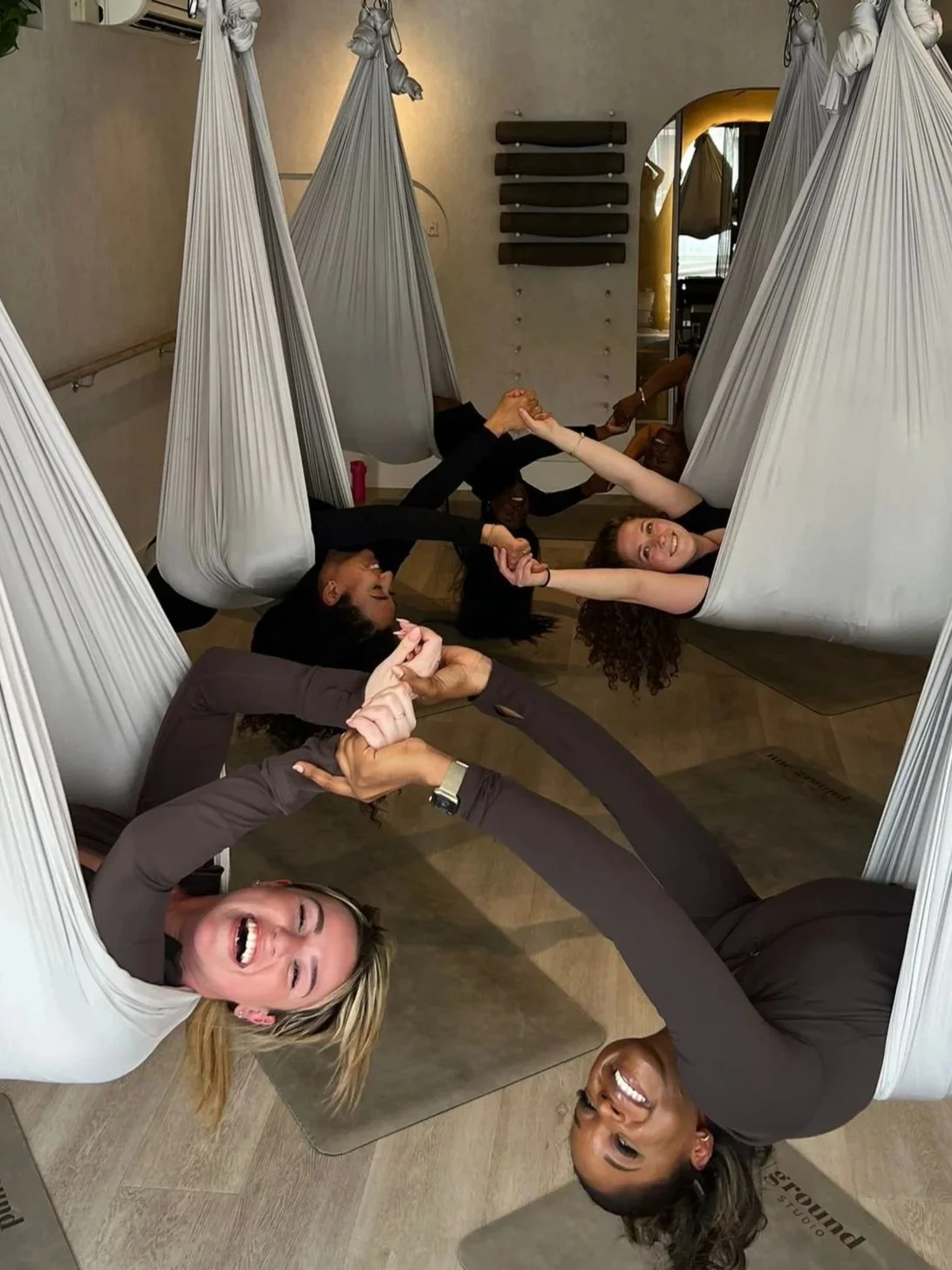 A smiling woman in exercise attire sitting on a yoga swing in a gym.