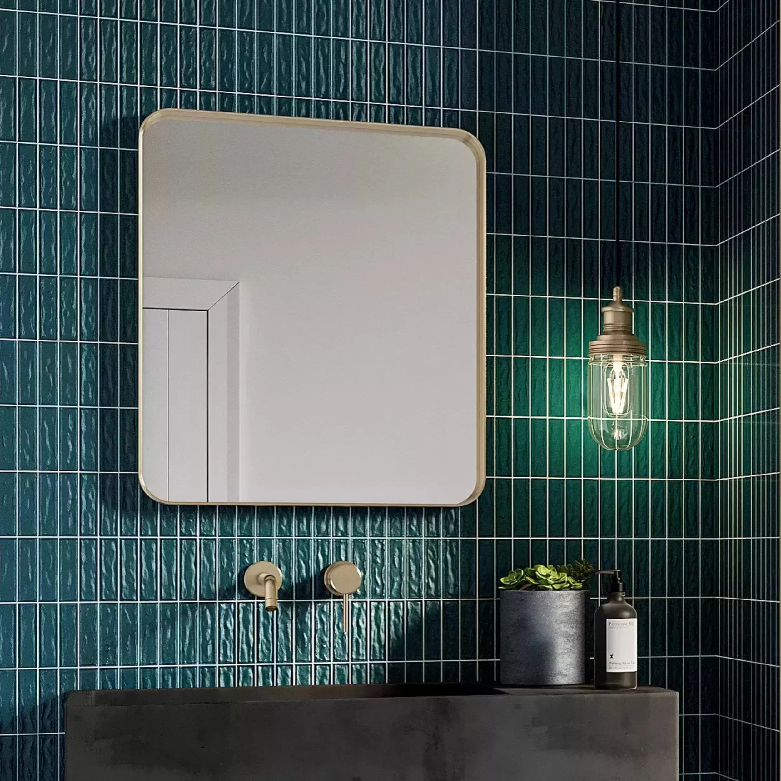 A bathroom with dark green tiled walls, a mirror, a bottle of skincare product, and a decorative plant on a black shelf.