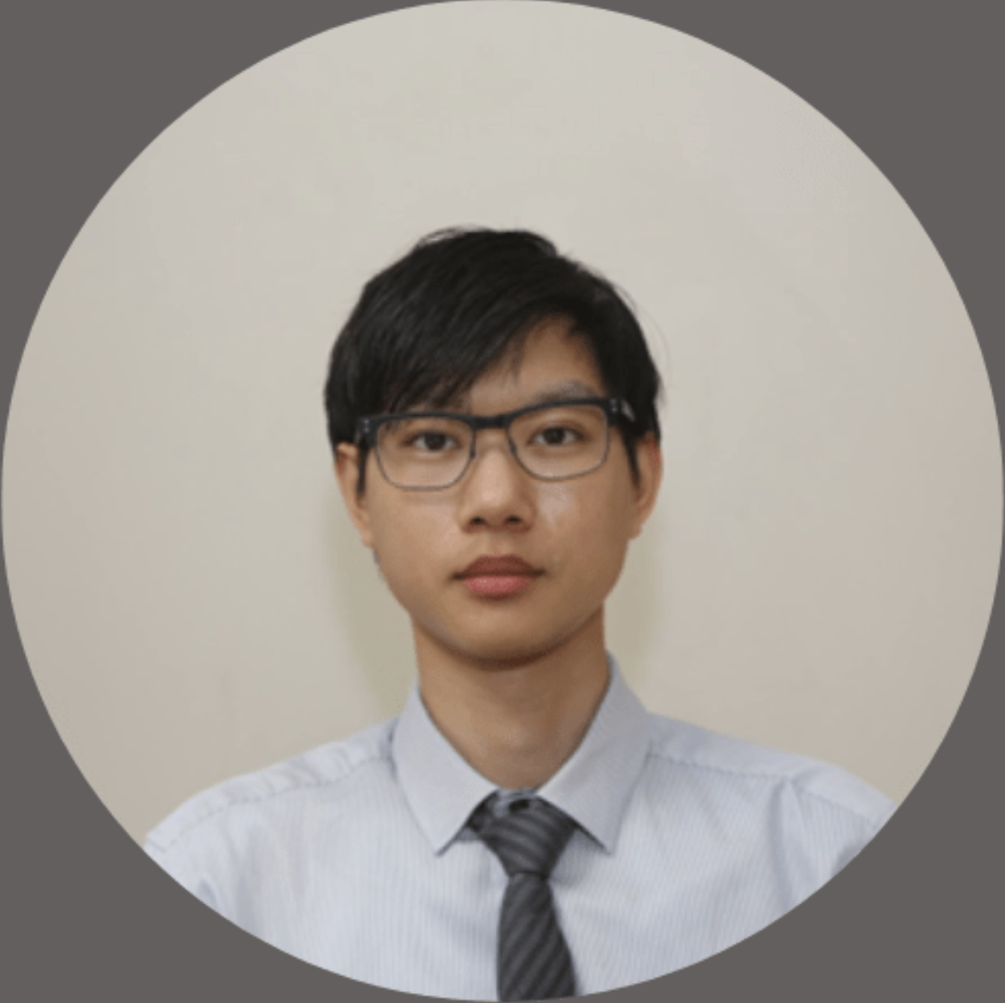 A young man with black hair and glasses wearing a light blue dress shirt and a dark striped tie against a plain light background.