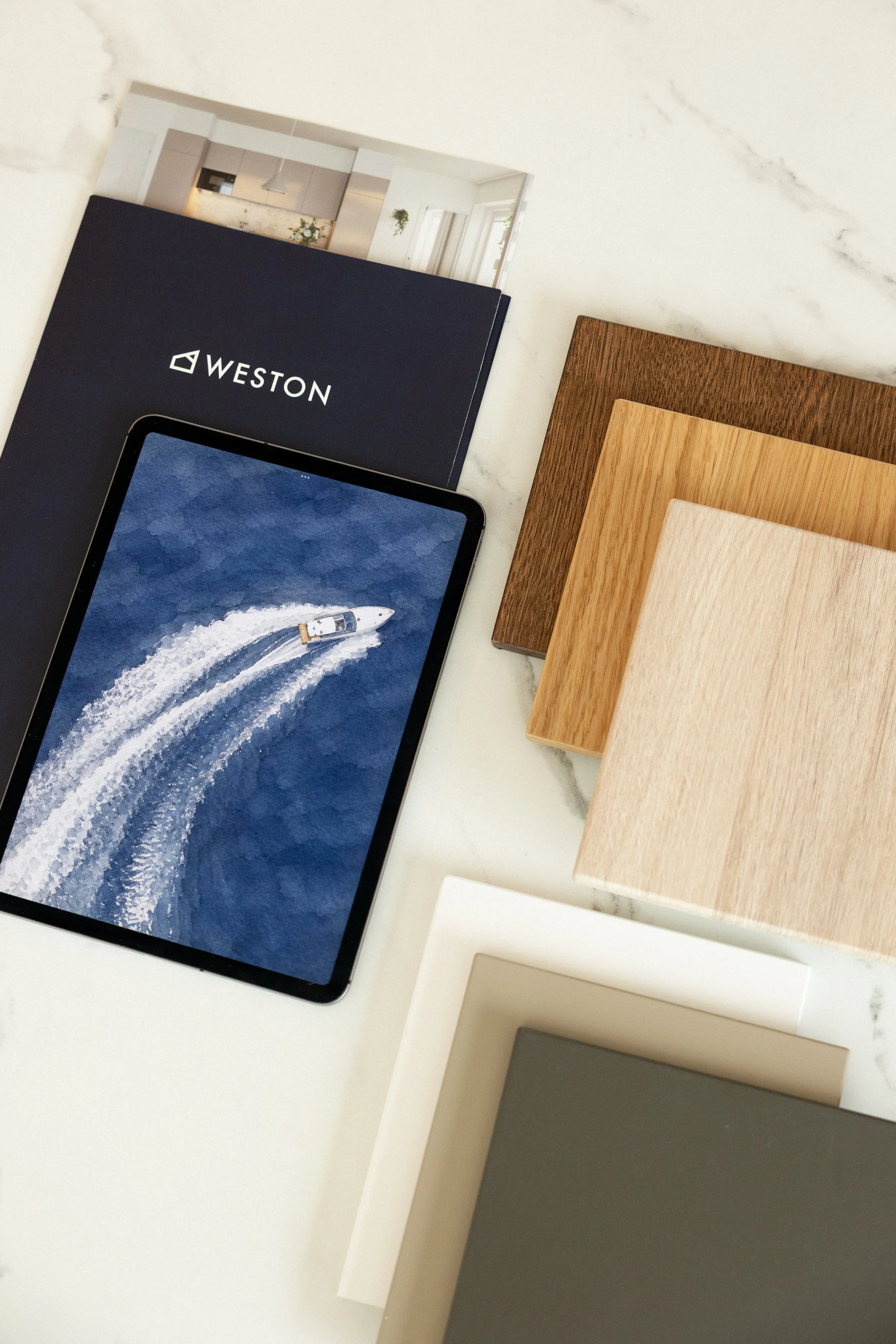 Weston Group. Kuvassa on tabletti ja puulevyistä tehtyjä näytteitä, lattiapintoja ja pintoja, jotka voivat olla sisustussuunnittelun tai materiaalinäytteiden näytteitä.
