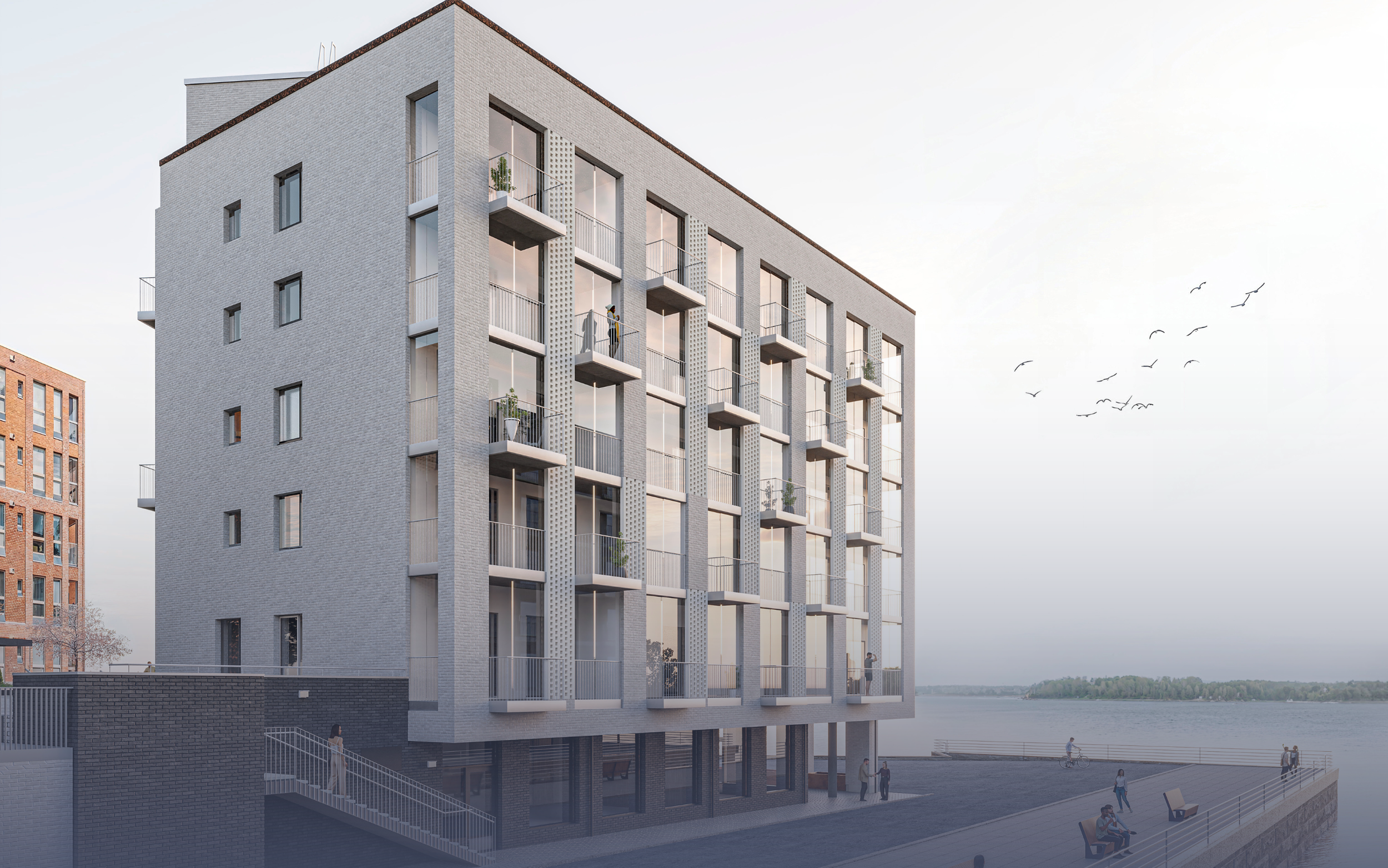 Kuvassa moderni kerrostalo meren rannalla, jossa on useita parvekkeita ja suuri ikkunapinta-ala. Lähellä rantaa on ihmisiä kävelemässä ja pyöräilemässä, taustalla näkyy meri ja taivasta ja muut rakennukset.