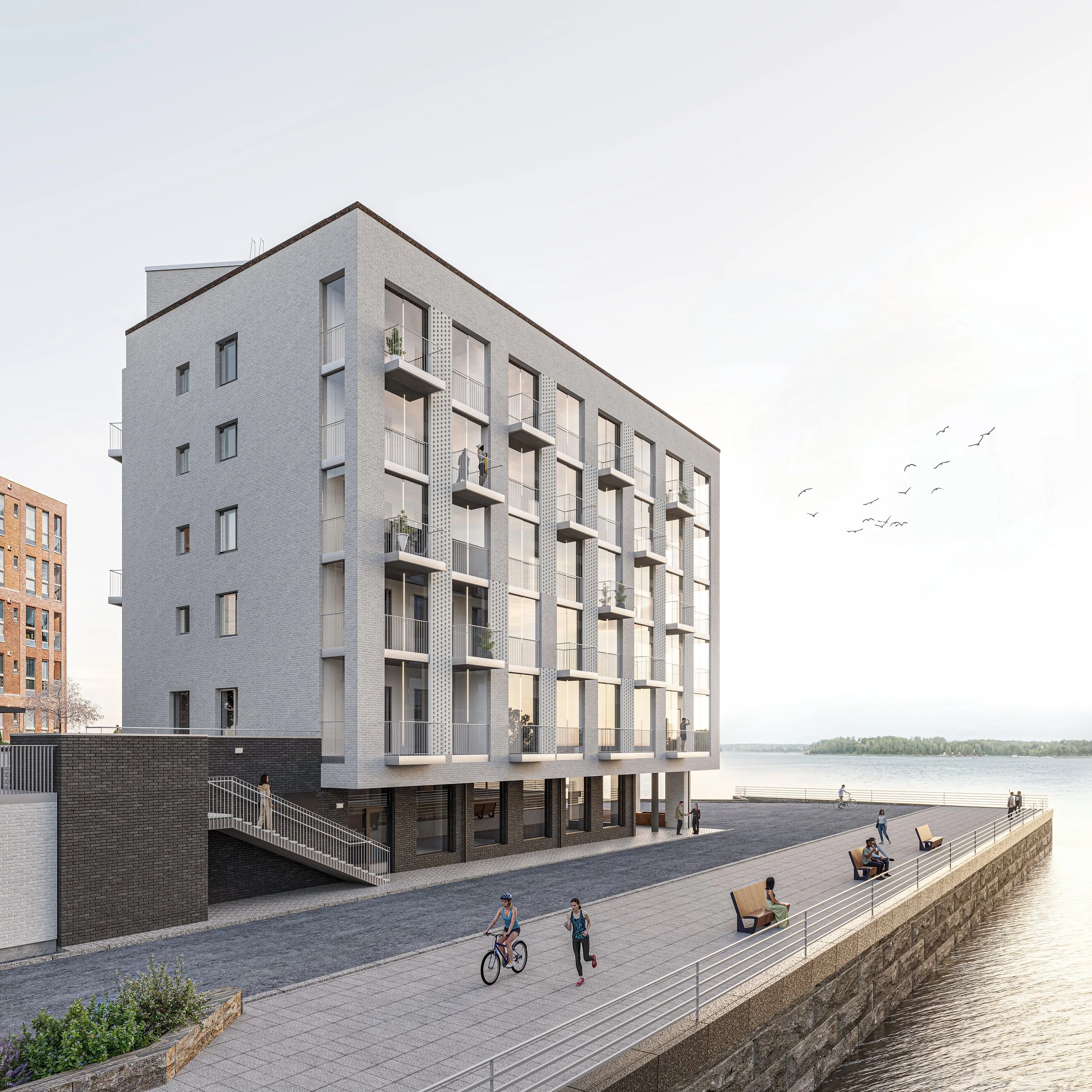 Kuvassa moderni kerrostalo sijaitsee veden äärellä. Rakennus on monikerroksinen ja siinä on parvekkeita. Alhaalla on kävelytie, joilla ihmiset kävelevät ja pyöräilevät. Vaimme eläviä ihmisiä ja laivoja taustalla.