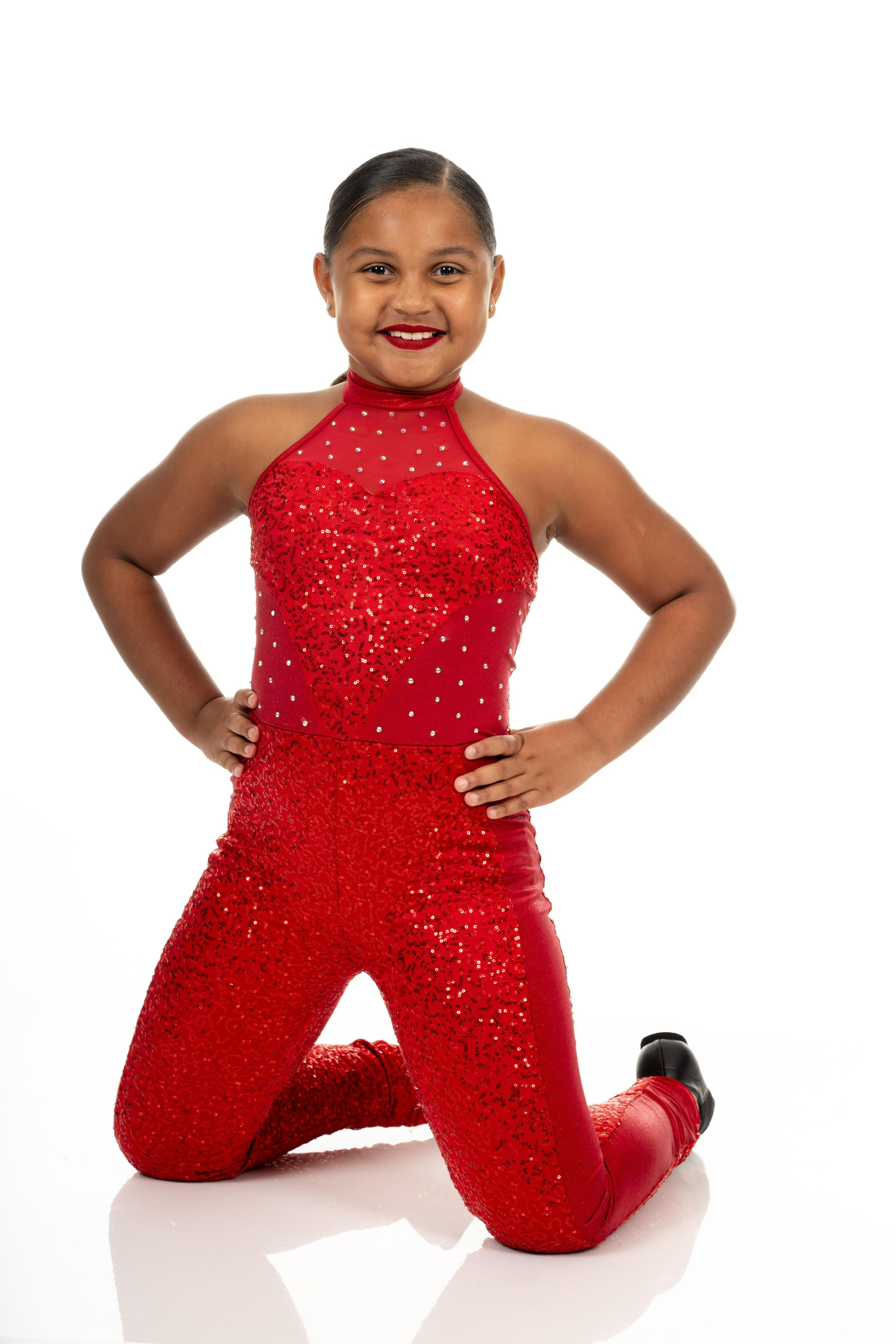 Angilique dressed in a red sparkly dance costume with matching red lipstick, posing confidently on her knees with hands on hips ready to do a jazz ensemble,