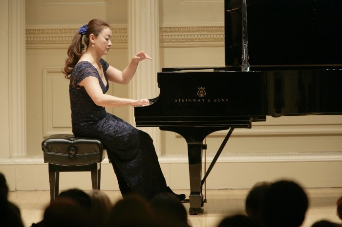 Young woman playing a grand piano on stage during a performance.