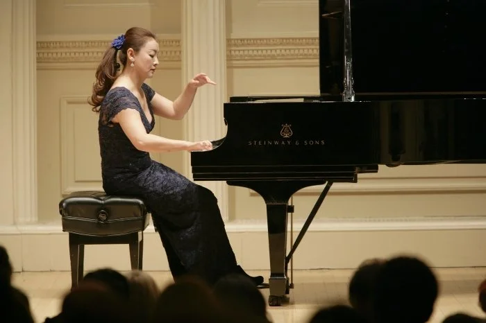 Winnie Wen in a black dress playing a Steinway & Sons grand piano on stage at Carnegie Hall.