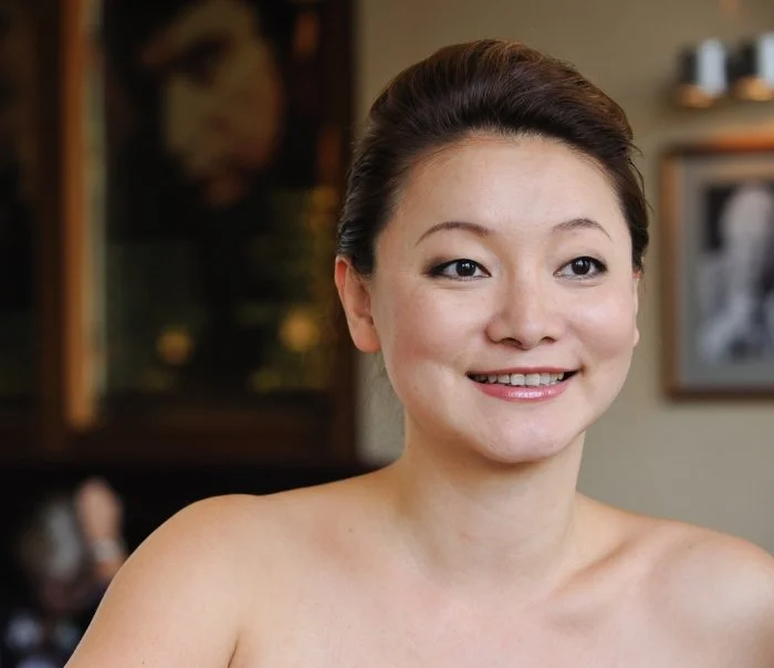 Winnie Wen smiling indoors, with artwork and shelves in the background.