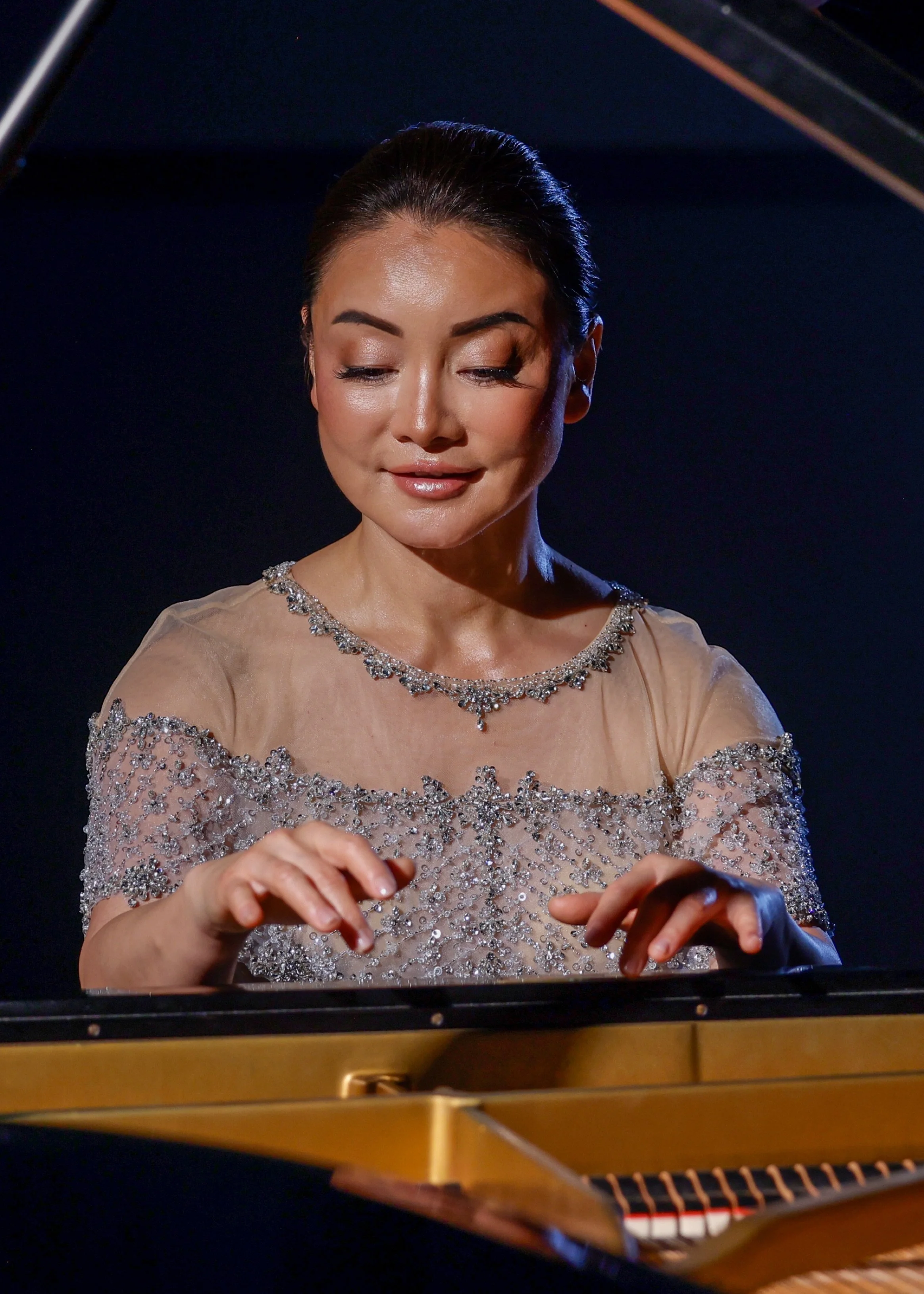 Winnie Wen playing the piano, wearing a gown with silver embellishments and focusing on her hands.