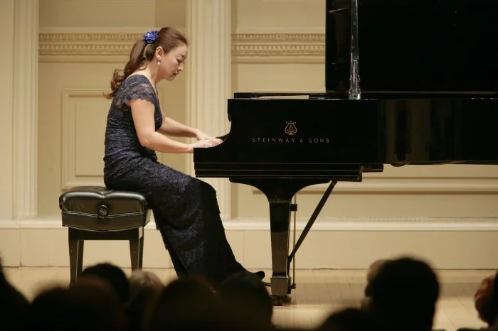 Young woman in a dark lace dress playing a black Steinway & Sons grand piano during a concert.