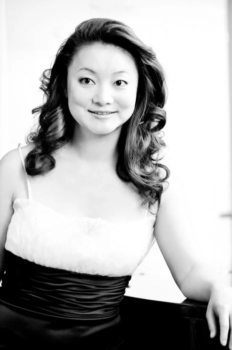 Winnie Wen smiling at the camera, wearing a sleeveless dress, in a black and white official performance portrait.