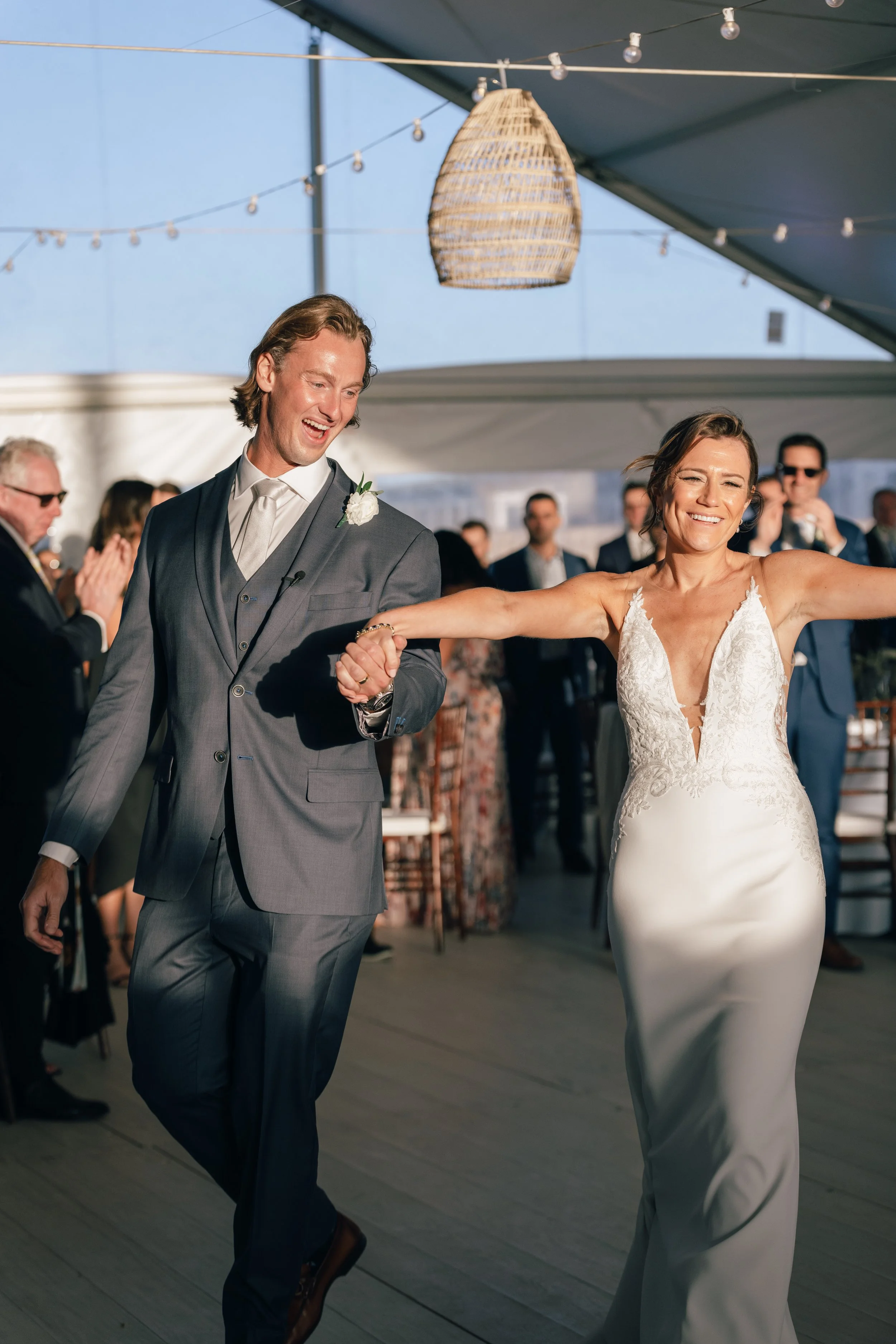 Galley Beach Wedding reception. A man and woman dance together at a wedding reception, smiling and holding hands, with guests in the background and string lights overhead.