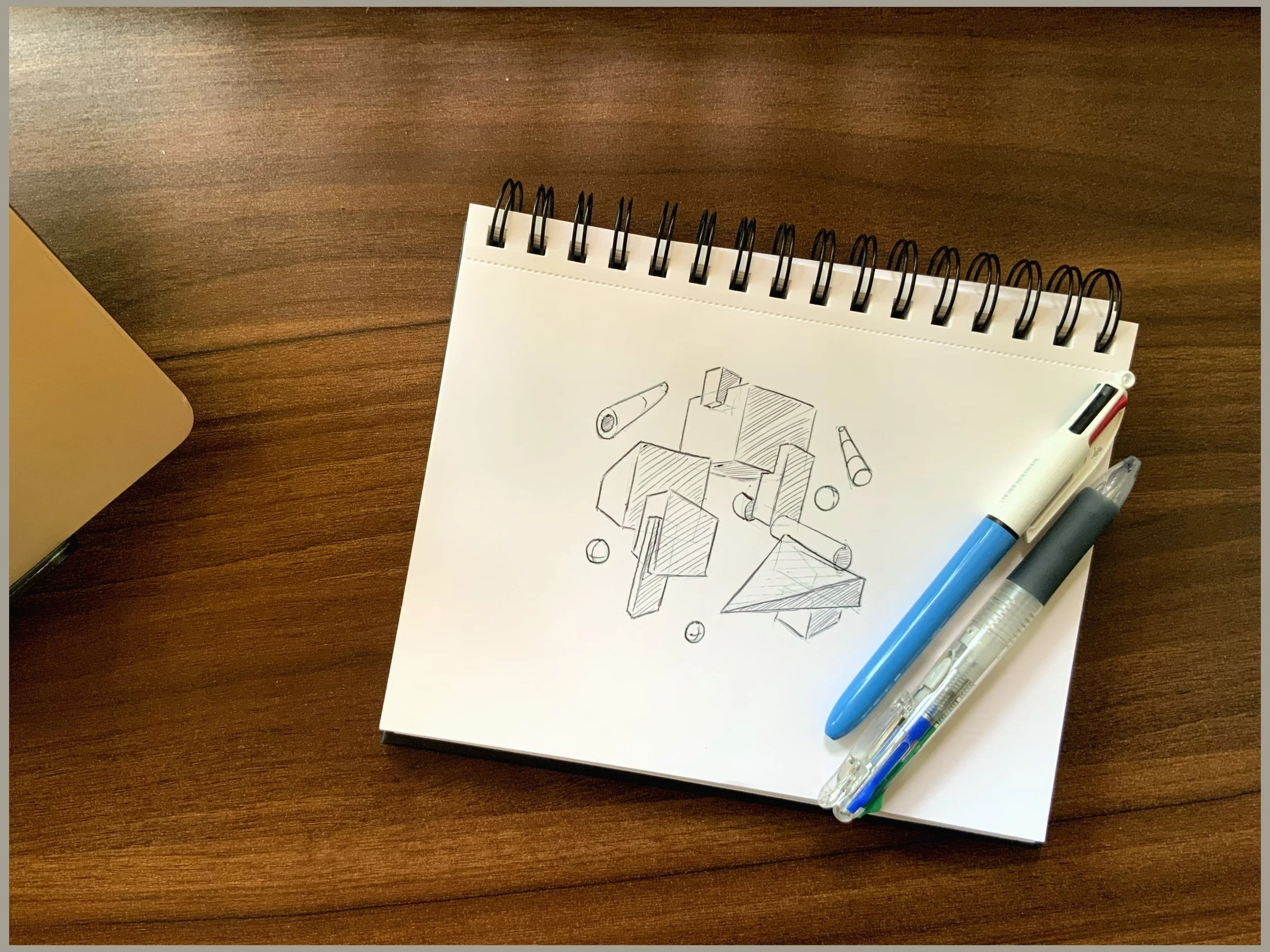 A sketchbook with architectural drawings, four pens, and a highlighter placed on a wooden desk.
