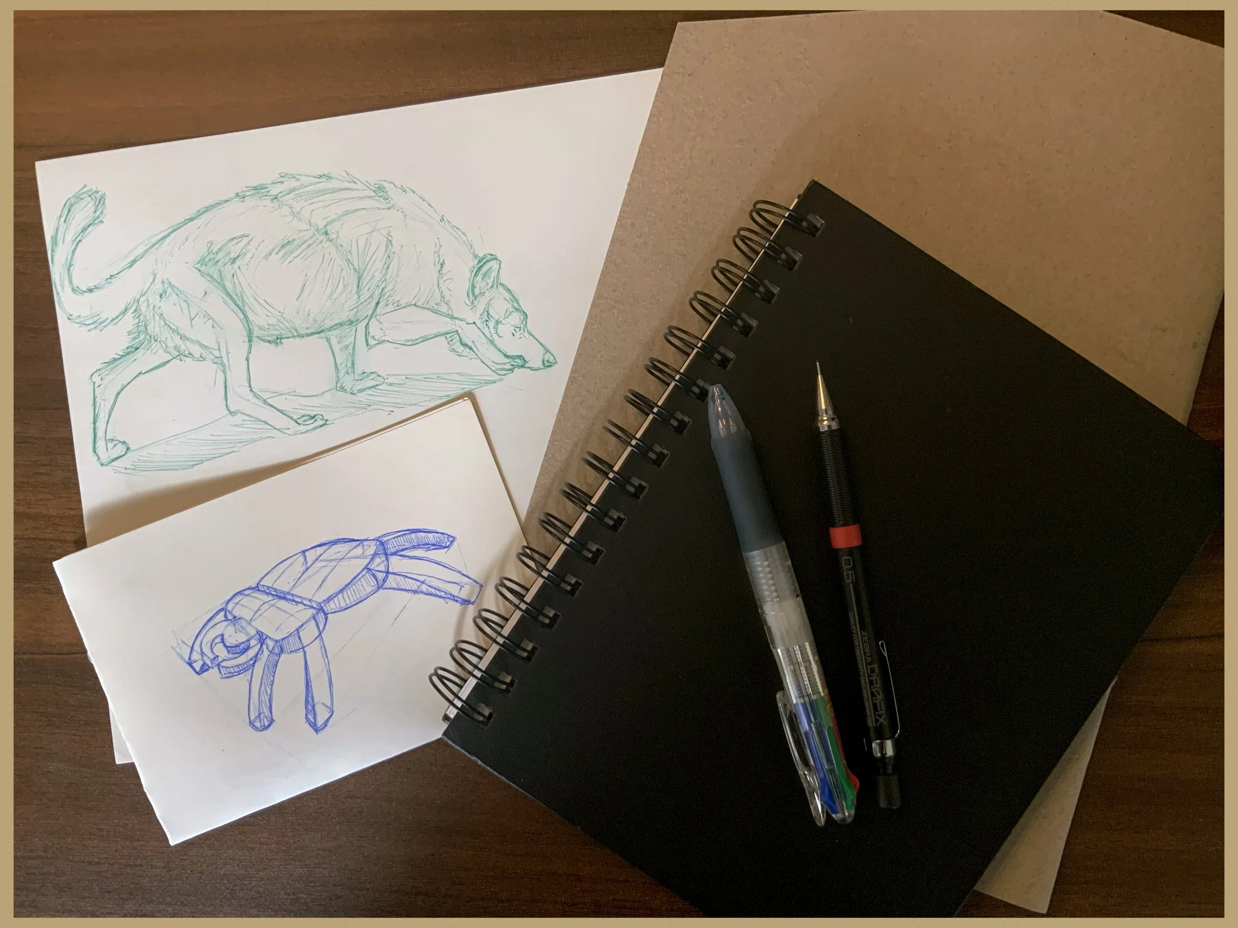 Sketches of fantasy creatures, including a dragon and a rat, on sheets of paper, with pens and notebooks on a wooden desk.