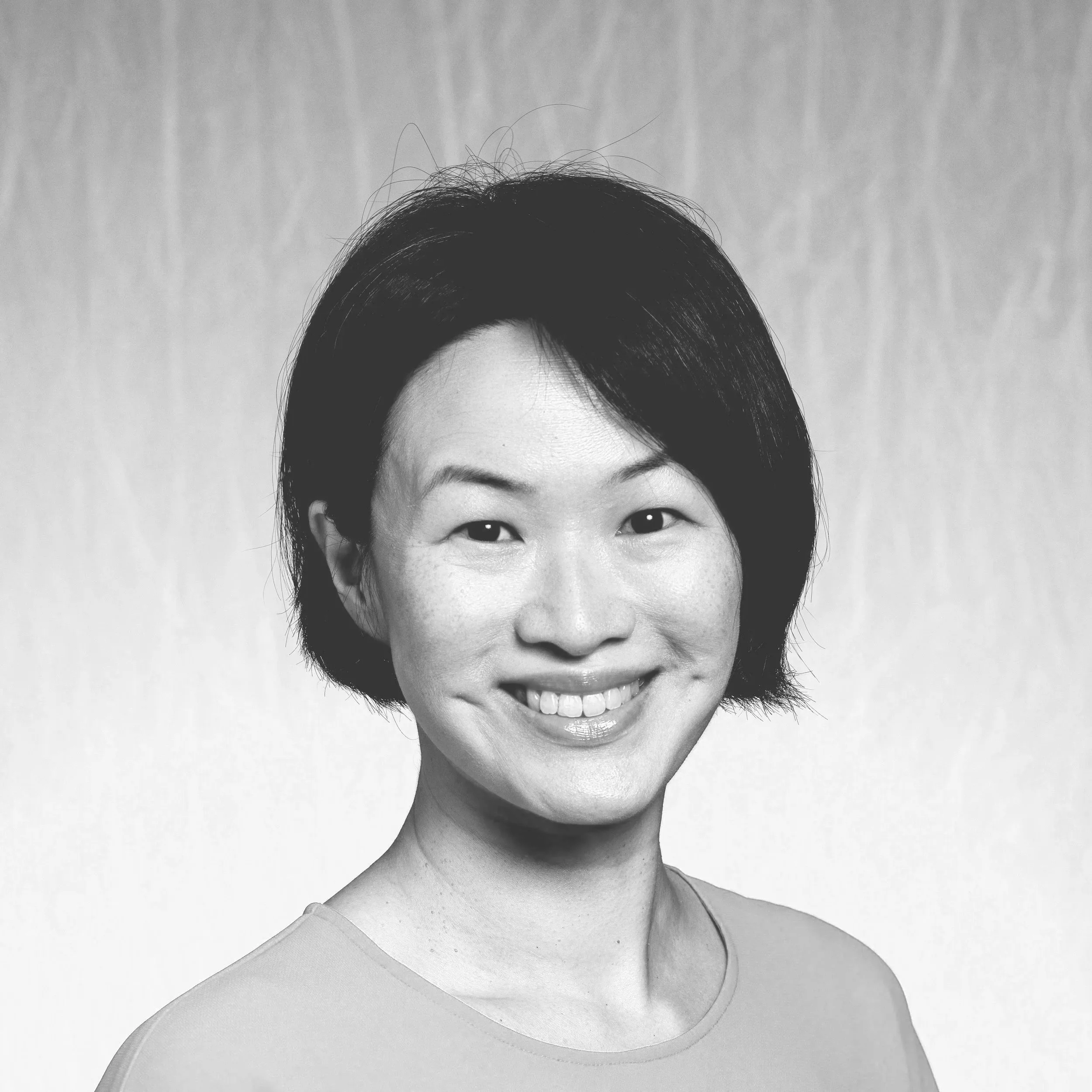 Black and white portrait of a woman with short hair smiling, wearing a top with a rounded neckline.