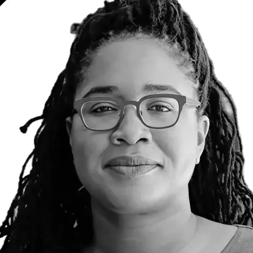 Close-up black-and-white portrait of a woman with glasses and long, textured hair, smiling softly.