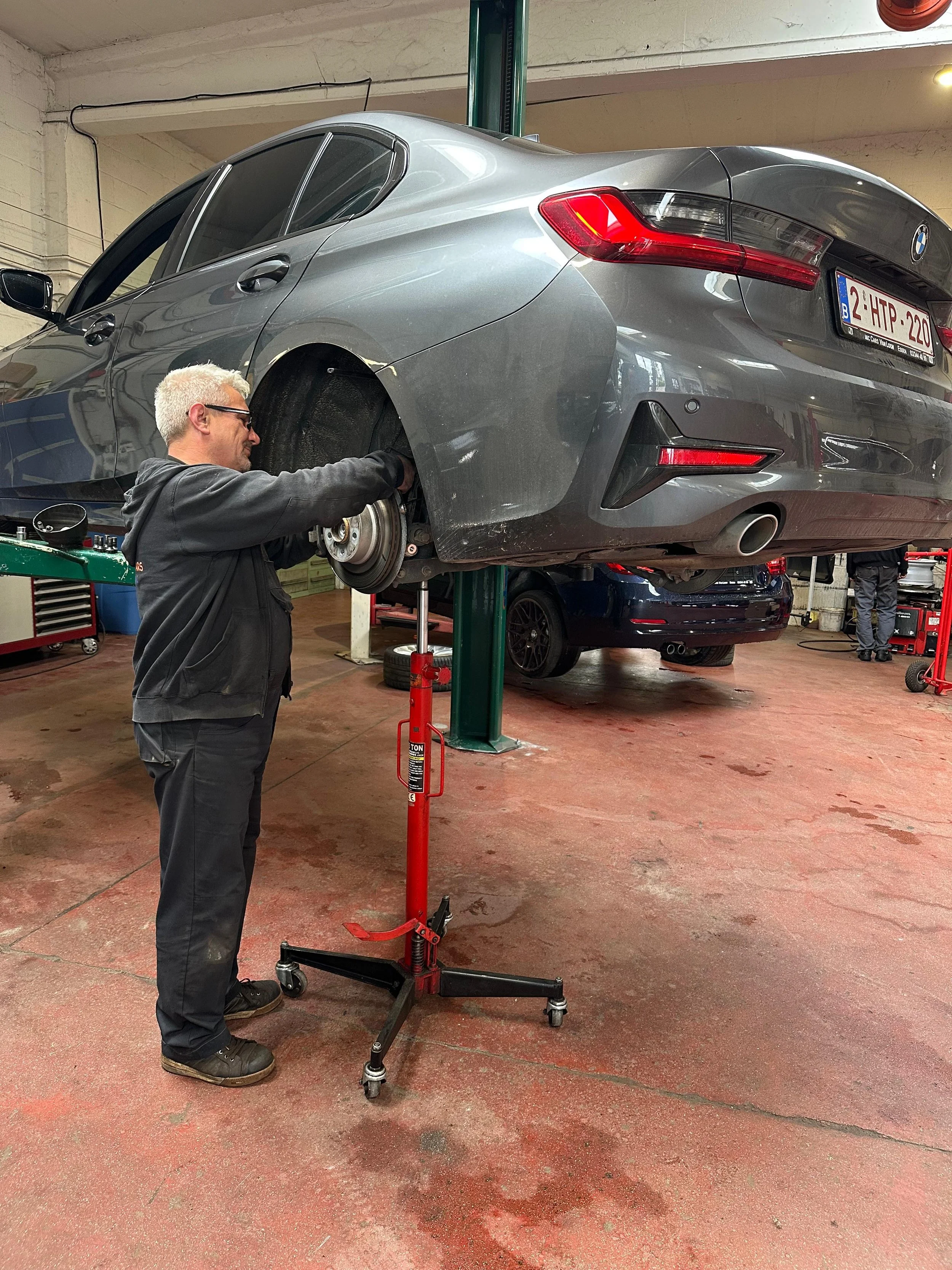 Man in een werkoutfit die een BMW-auto omhoog tilt op een carlift in een werkplaats.