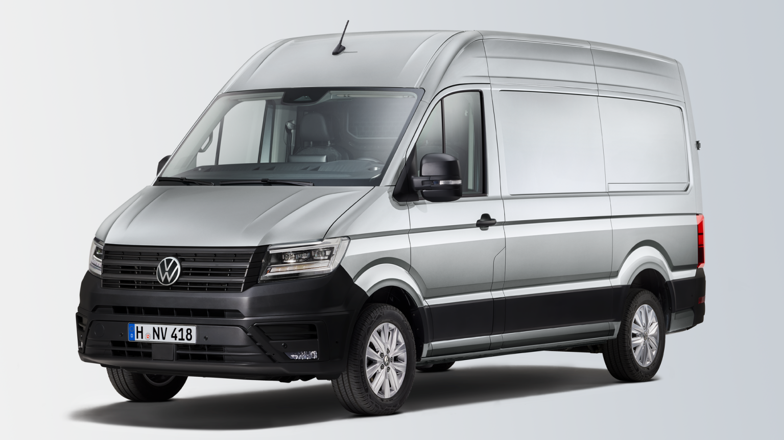 Een zilverkleurige Volkswagen bedrijfswagen met een hoge opbouw, donkere voorbumper en zijspiegels, tegen een witte achtergrond.