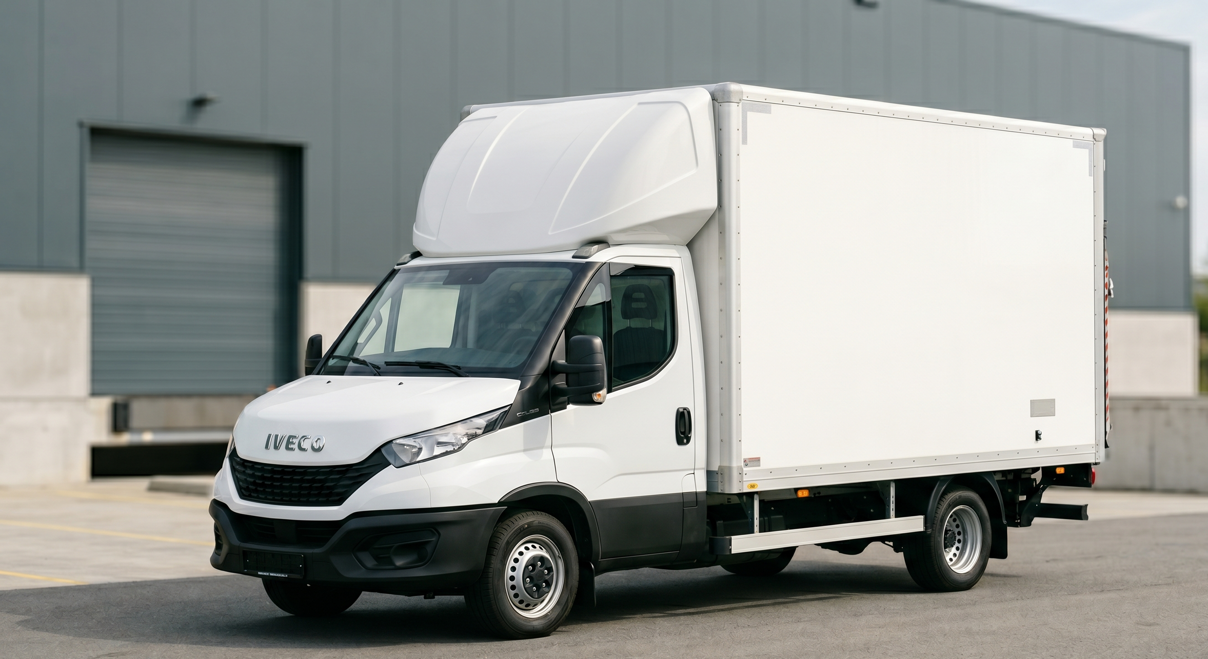 Een witte bezorgtruck van het merk Iveco geparkeerd buiten een industrieel gebouw.