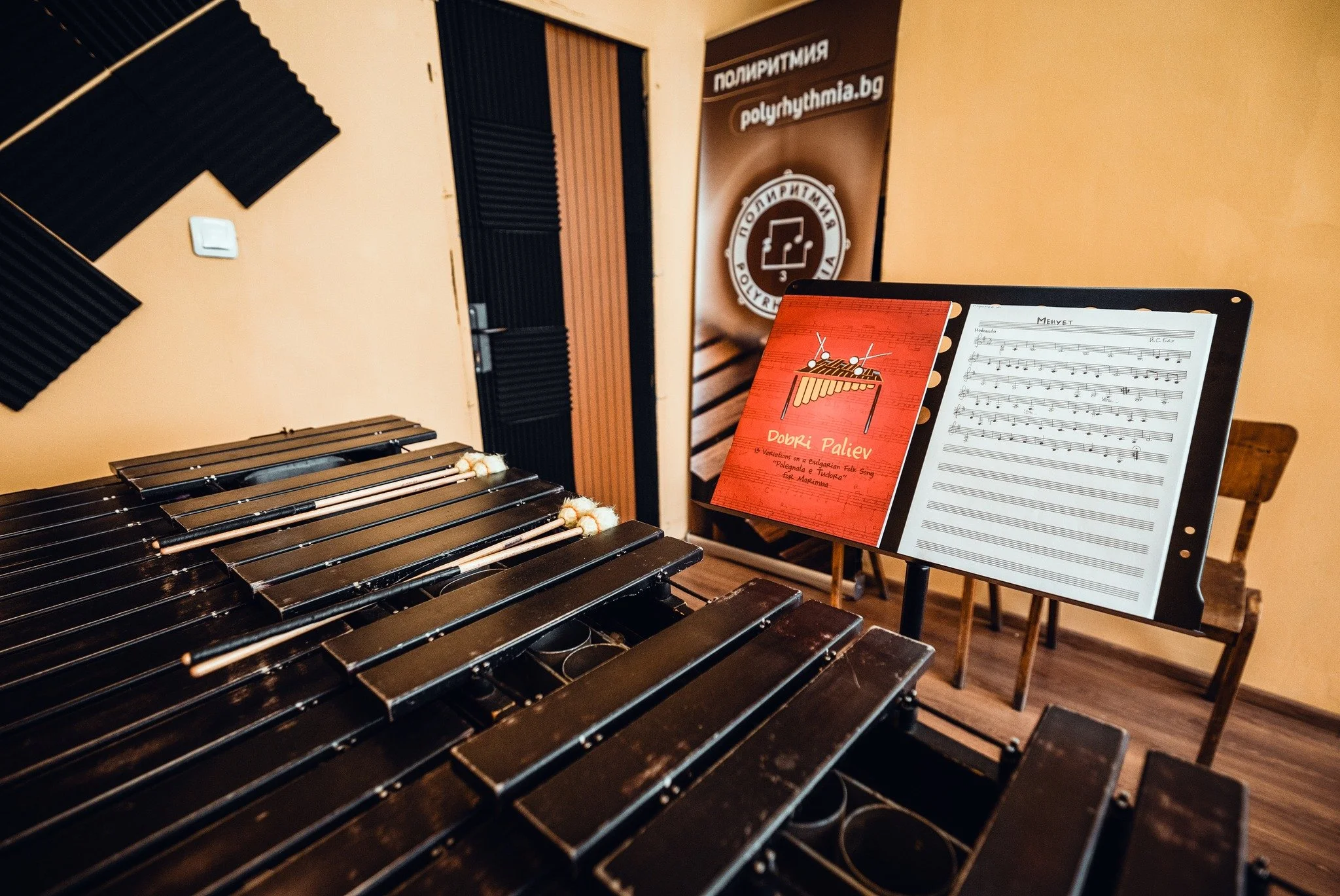 A music studio room with a wooden keyboard, soundproofing foam panels on the wall and a music sheet stand with sheet music and a red booklet.