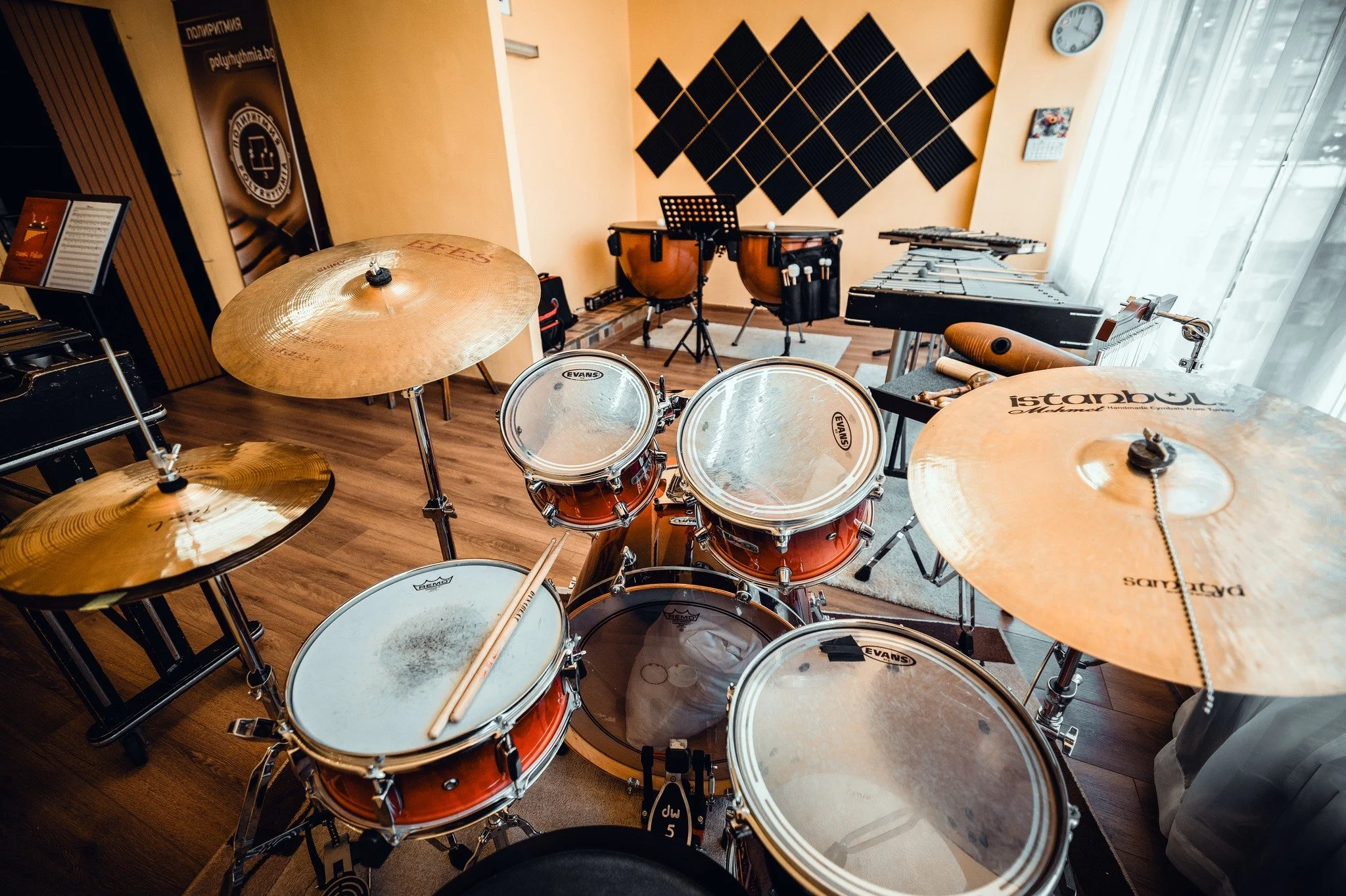 A music practice room with various instruments, including drums, vibraphone, timpani, and a poster on the wall.