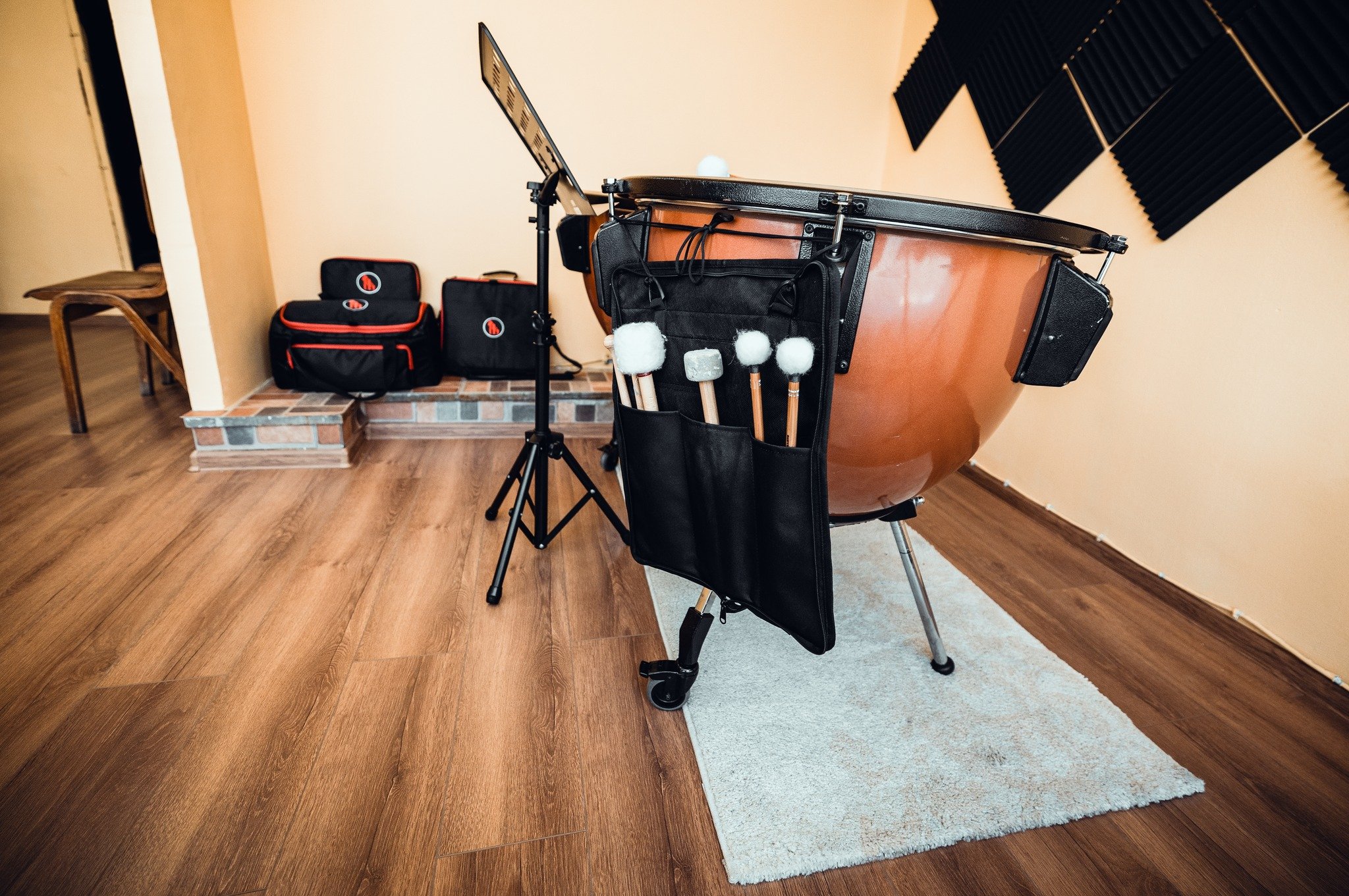 Recording studio with a large timpani drum, soundproofing foam panels on the wall, and music equipment bags on a raised platform.