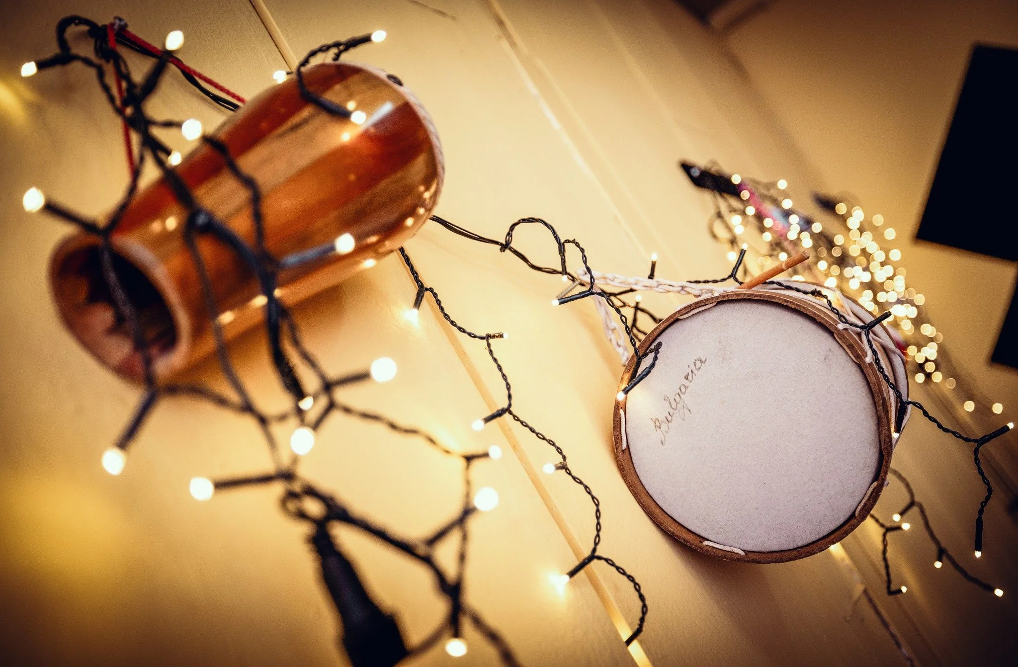 Close-up of a wooden drum with handwriting inside, surrounded by a string of small white LED fairy lights, on a wooden surface.