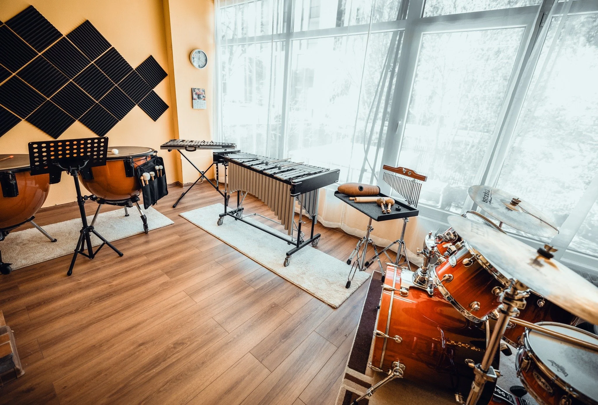A music practice room with musical instruments and soundproofing foam on the walls, large windows with curtains, and sunlight coming in.