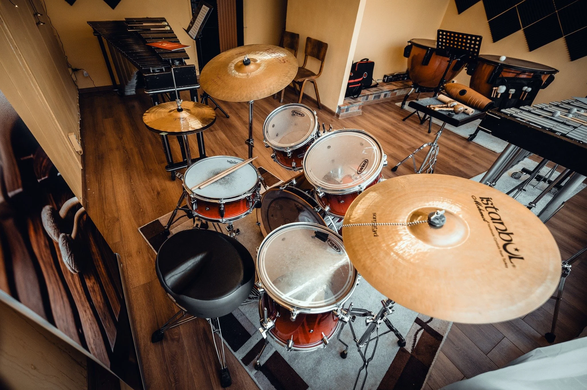 A music studio with various musical instruments including drums, xylophone, and other percussion instruments arranged on a wooden floor.