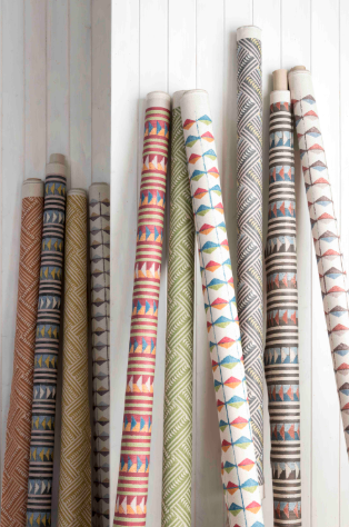 A collection of rolled-up patterned wallpaper rolls standing vertically against a white wooden wall.