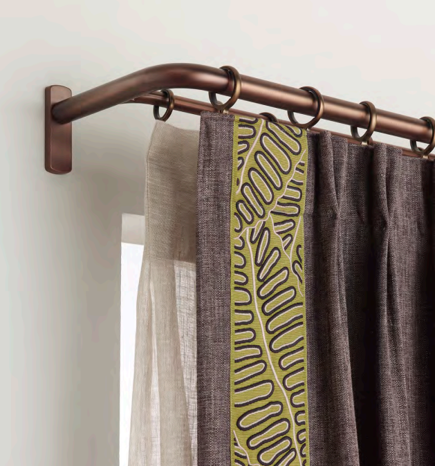 Close-up of a copper-colored curtain rod holding four curtains, with a plain beige curtain, a patterned curtain with yellow and gray design, and two textured dark gray curtains.