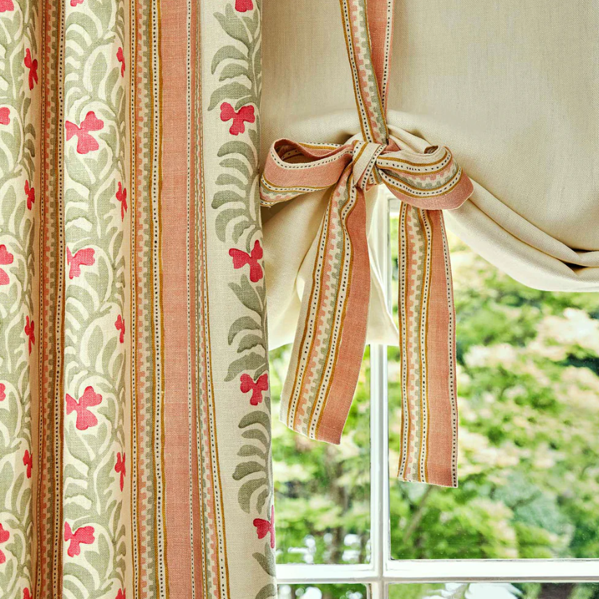 Close-up of patterned curtains tied back with a matching fabric tie, with a window and green foliage outside.