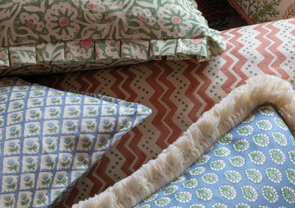 Close-up of decorative pillows with floral and geometric patterns, featuring different colors and textures, on a bed.