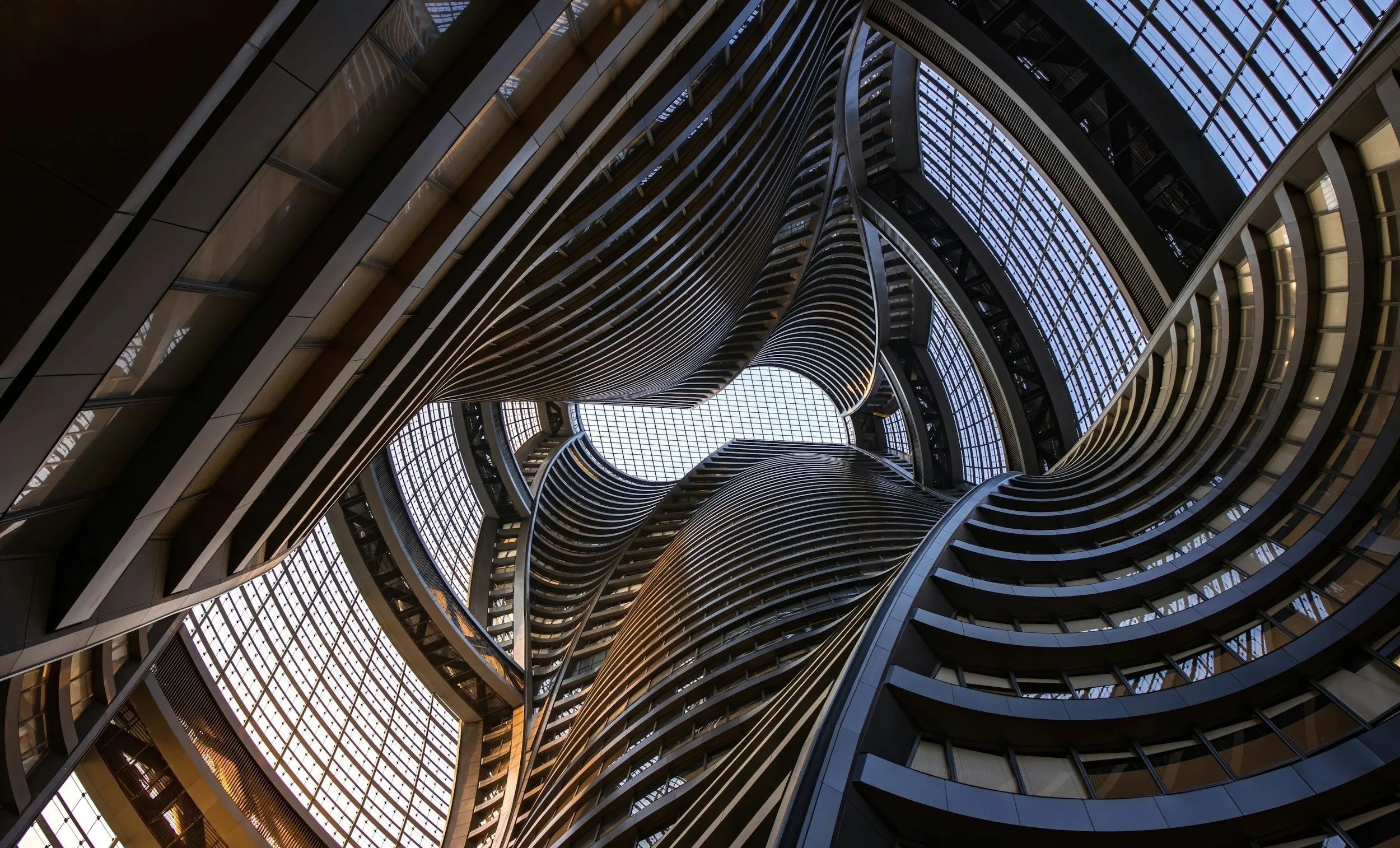 Interior view of a modern multi-story building with curved balconies and glass ceilings, looking upward.