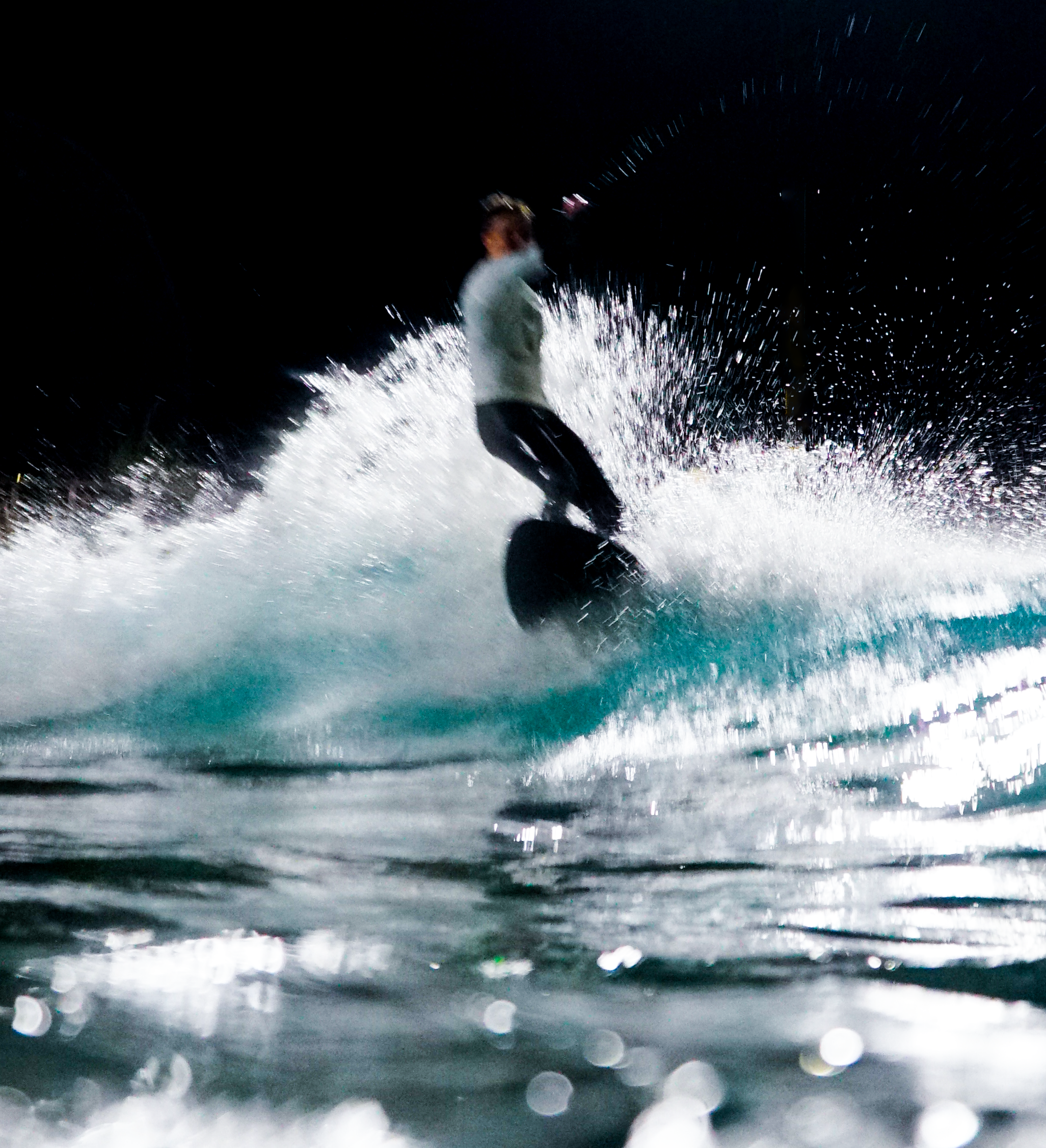A person surfing on a wave at night, with water splashing around and star-like reflections on the water surface.