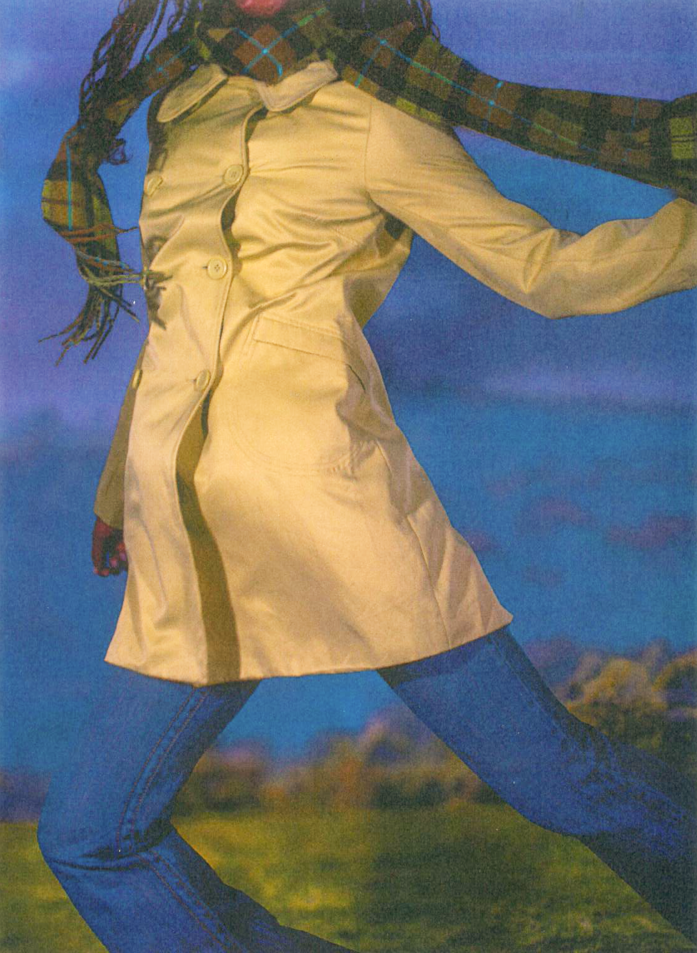A woman wearing a beige trench coat, dark pants, and a plaid scarf standing outdoors with her hand on her head, against a blue sky background.