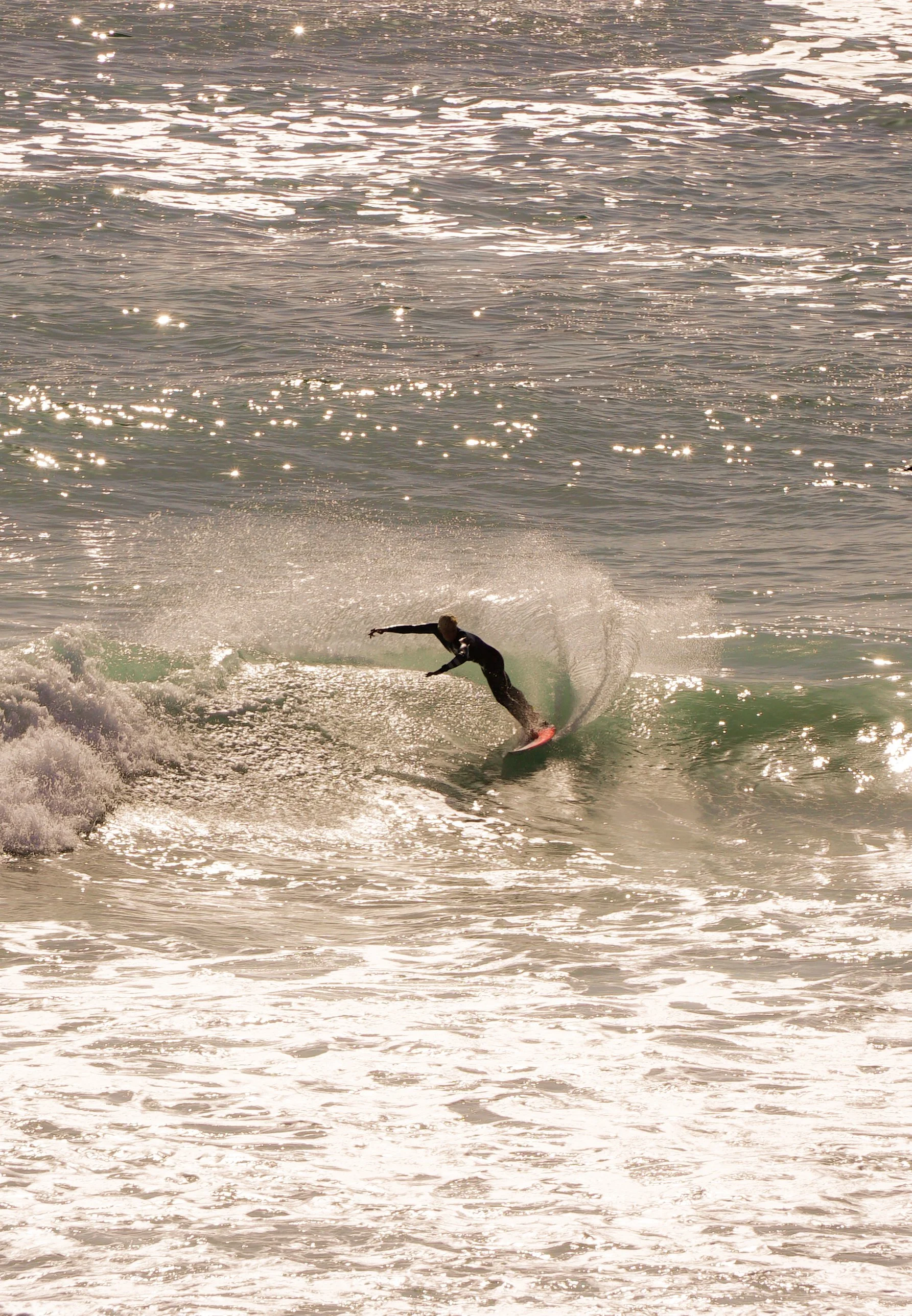 A person surfing on a wave in the ocean at sunset, with sunlight reflecting off the water