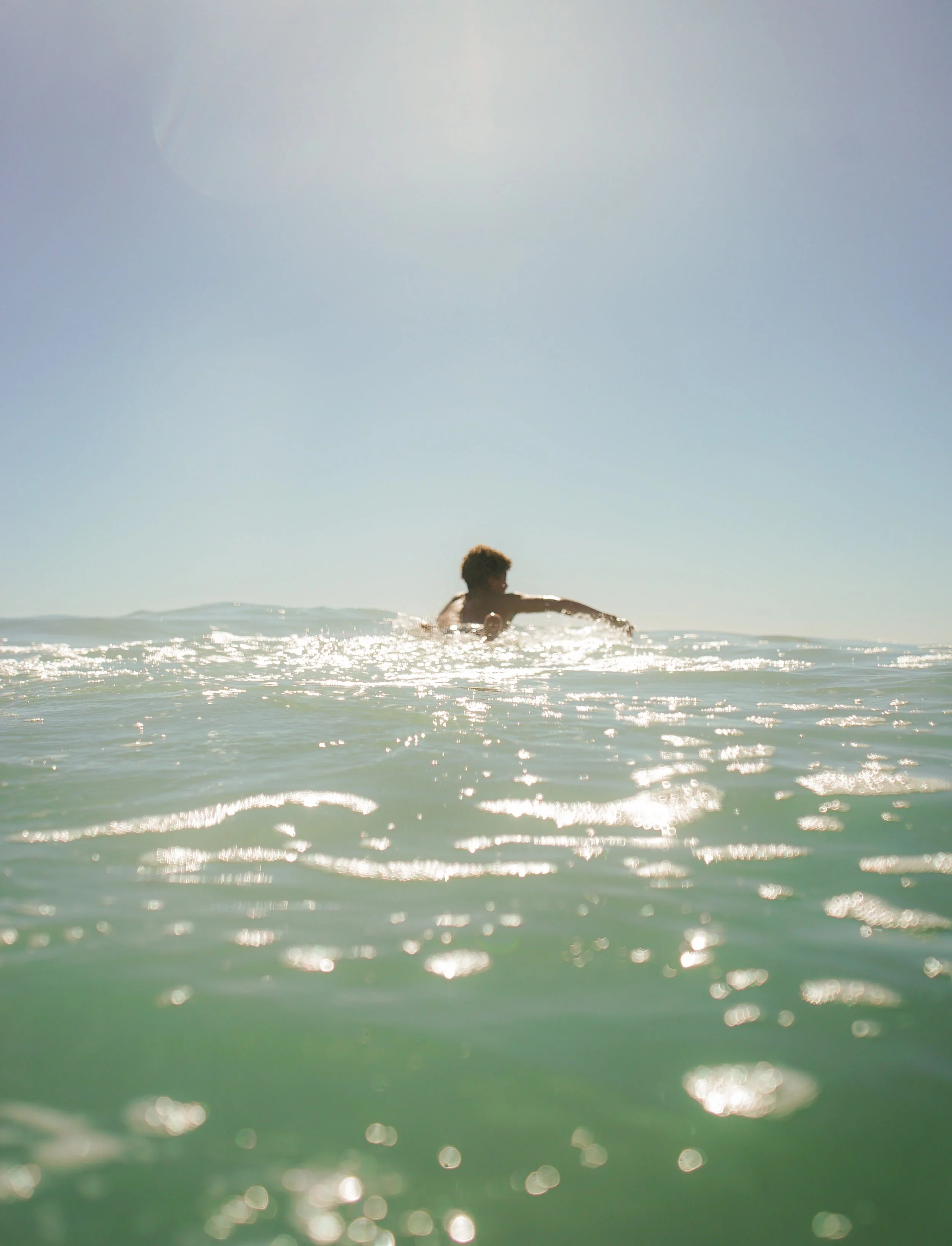 Person surfing on a wave in the ocean during sunlight.