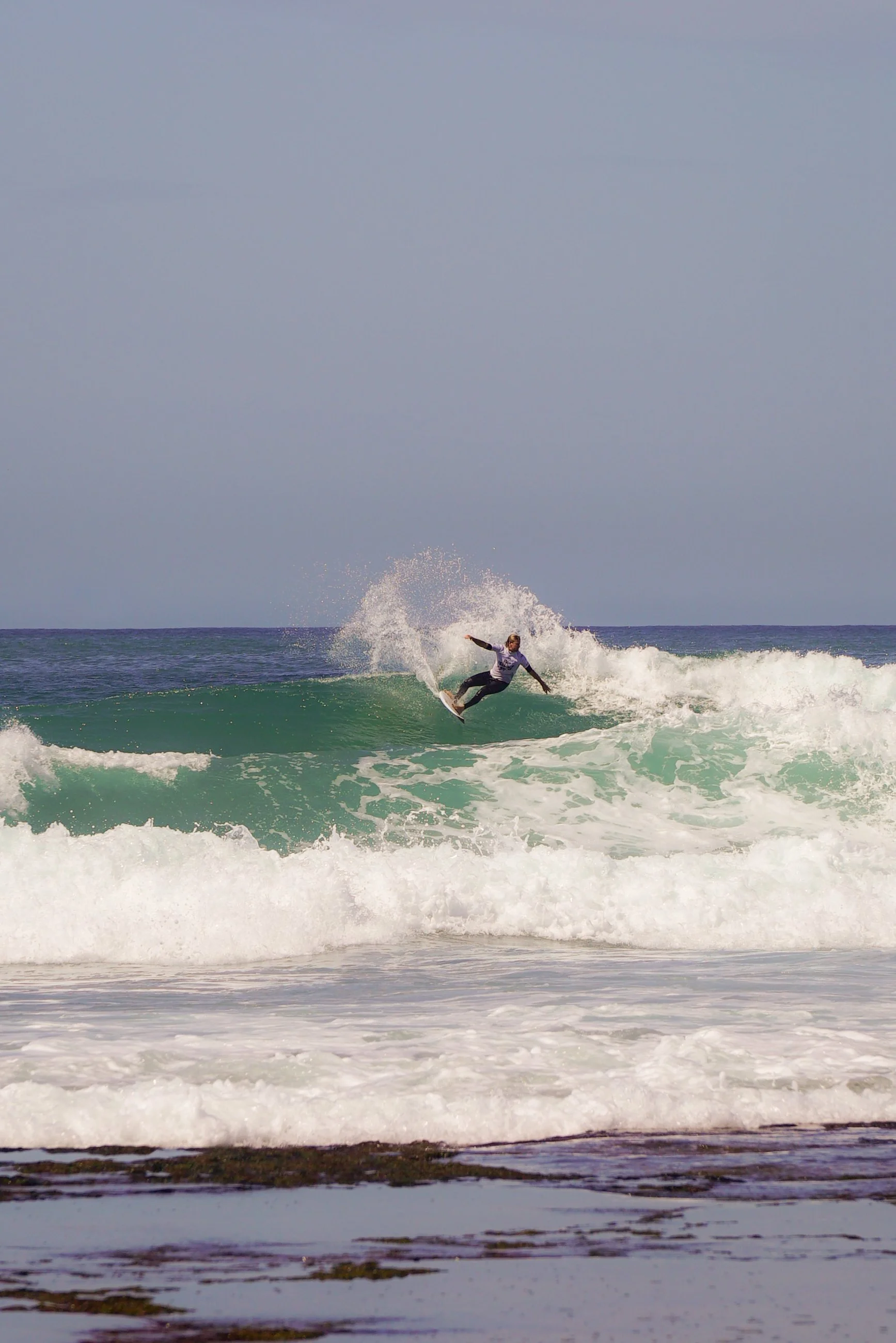 A person surfing on a wave at the beach under a cloudy sky.