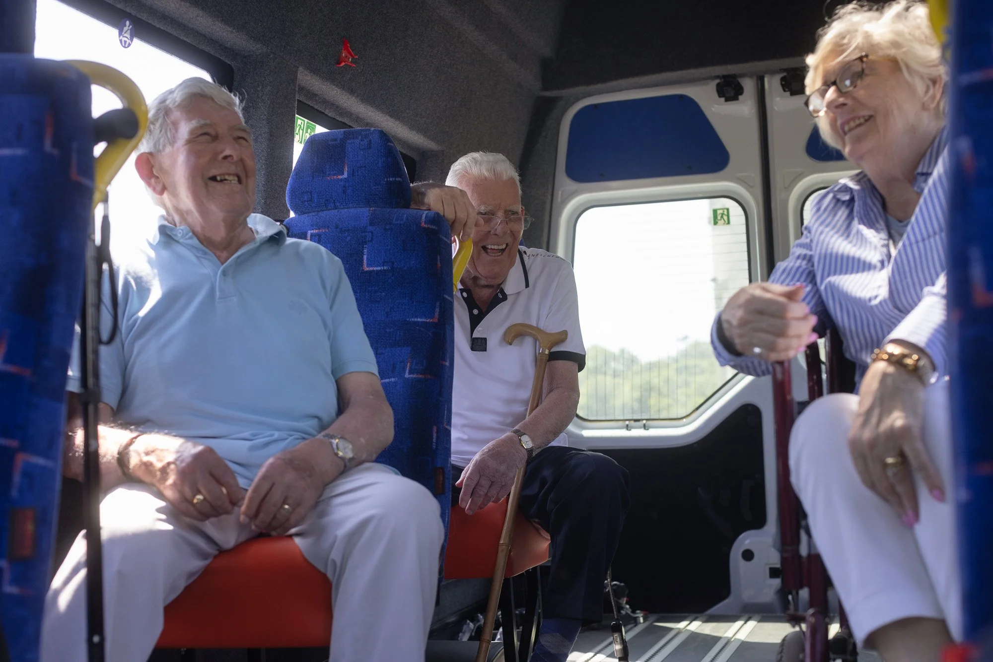 Senior men and women sitting and smiling inside a bus, enjoying a conversation.