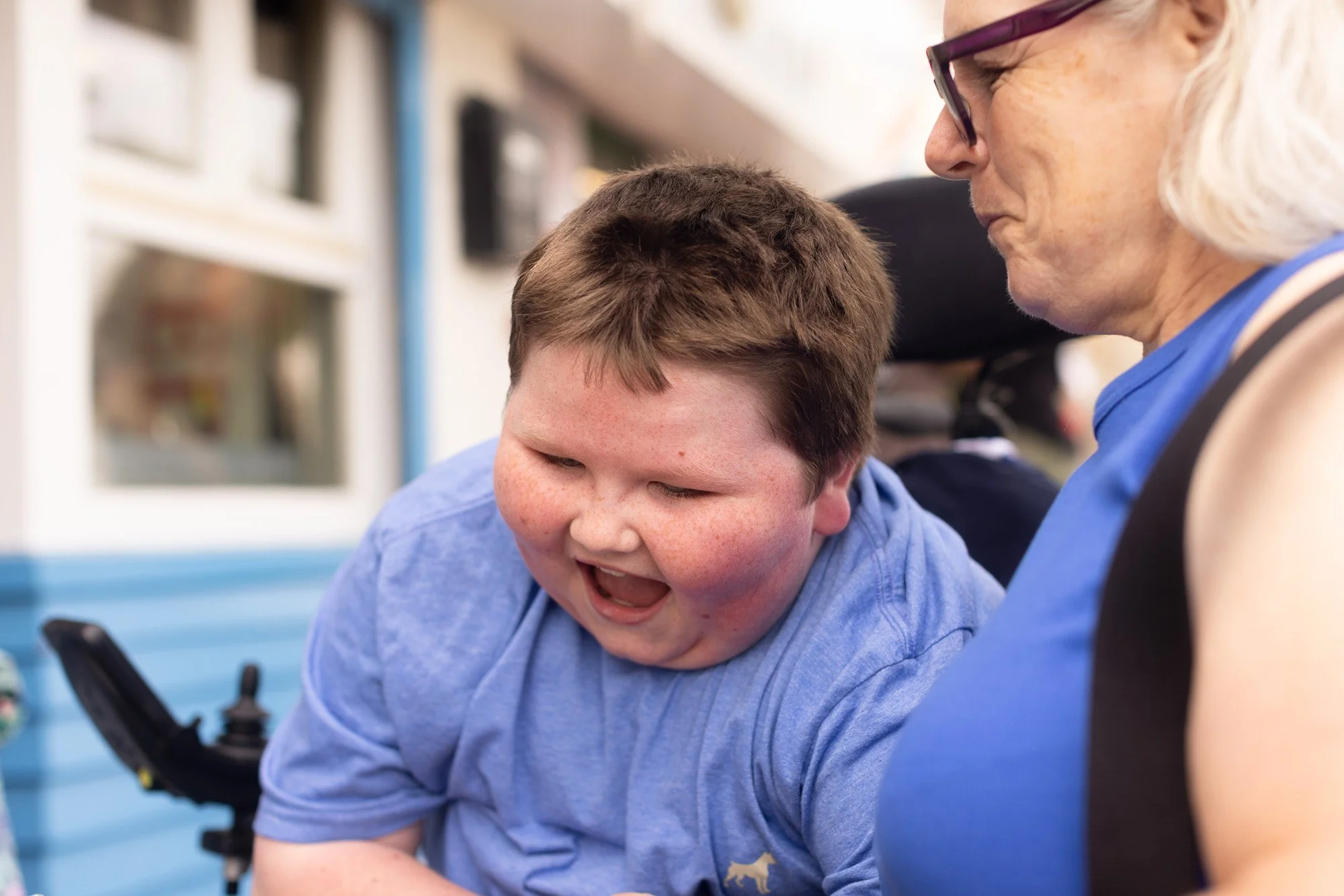 An elderly woman and a young boy are engaging with a device or screen, with the woman looking at it and the boy appearing excited or happy.
