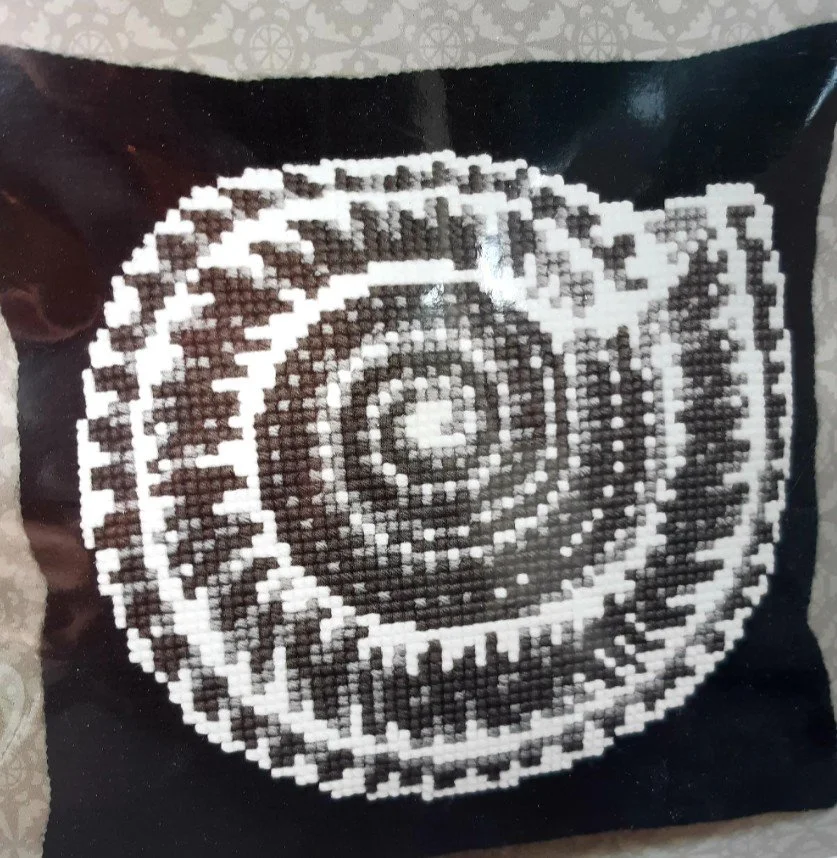 Mustavalkoinen kirjottu tyyny, jossa on pyöreä, spiralimainen kuvio.