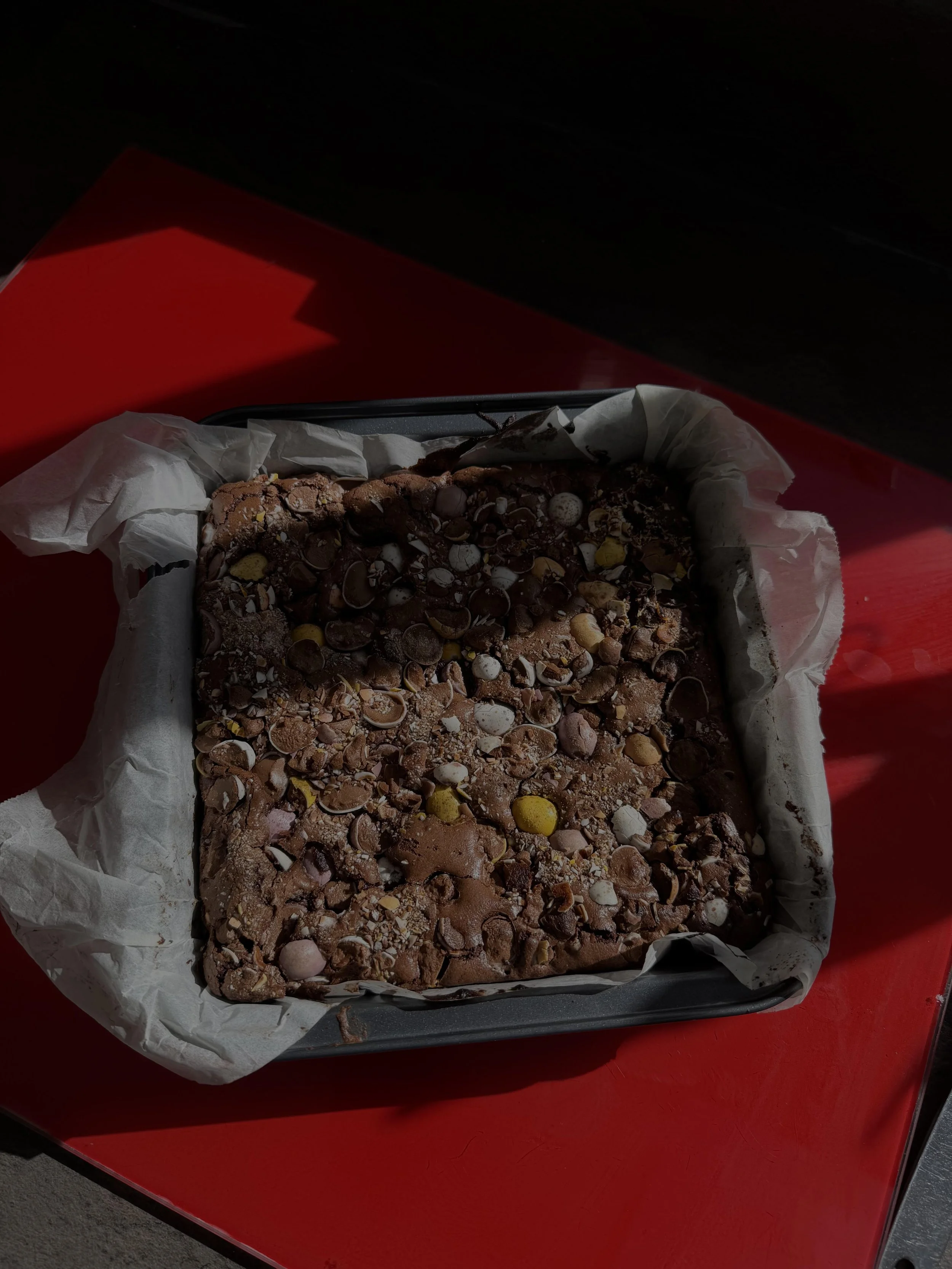 Chocolate cake with assorted candies and sprinkles in a baking dish lined with parchment paper.