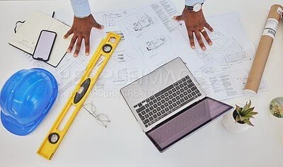 Architectural plans, a laptop, a hard hat, a spirit level, a notebook, a smartphone, a plant, and blueprints on a white table