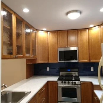 Kitchen with wooden cabinets, a microwave oven, a stove, a white countertop, and a sink.