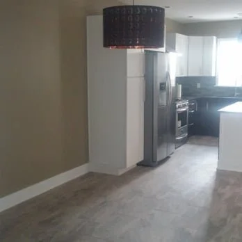 Empty kitchen with stainless steel refrigerator, microwave, oven, white cabinets, and beige walls.
