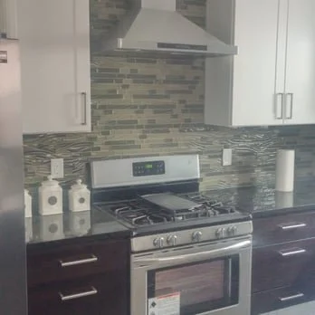 Modern kitchen with stainless steel stove, gray mosaic backsplash, white cabinets, and black lower cabinets.