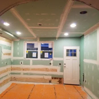 Room under renovation with green drywall, a window, and a door, with unfinished walls and ceiling.