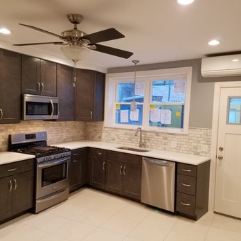 Modern kitchen with dark wood cabinets, stainless steel appliances, a white subway tile backsplash, a large window, and an air conditioning unit. Ceiling fan with lights is also visible.