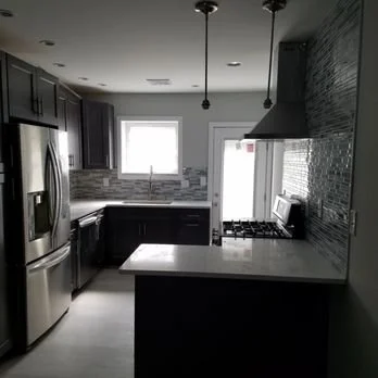 Modern kitchen with dark cabinets, stainless steel appliances, a window, and pendant lights