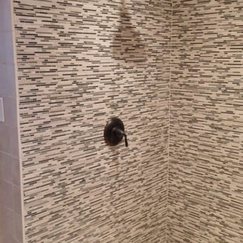 Close-up of a shower wall with a bronze shower handle and textured tile design.