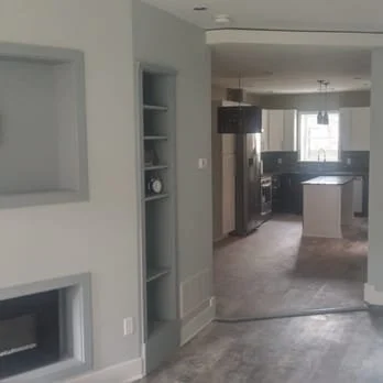 View of a modern kitchen and dining area with light gray walls, a built-in shelf, and large windows letting in natural light.